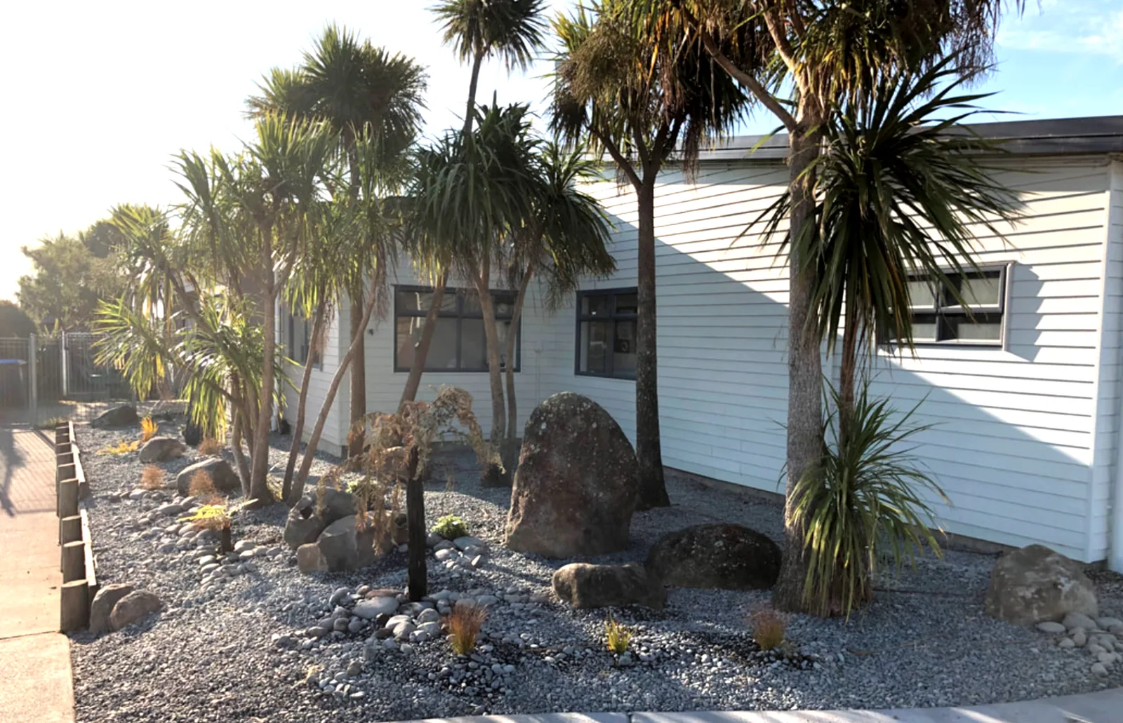 Landscaped garden bed with cabbage trees and rock edging beside a house