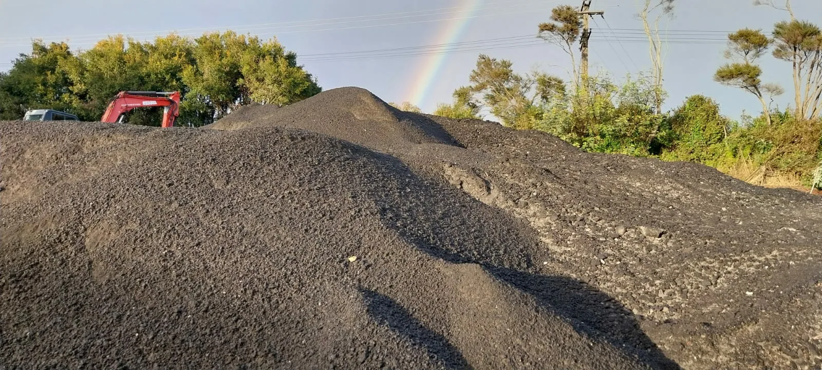 Stockpile of recycled asphalt millings with a rainbow behind