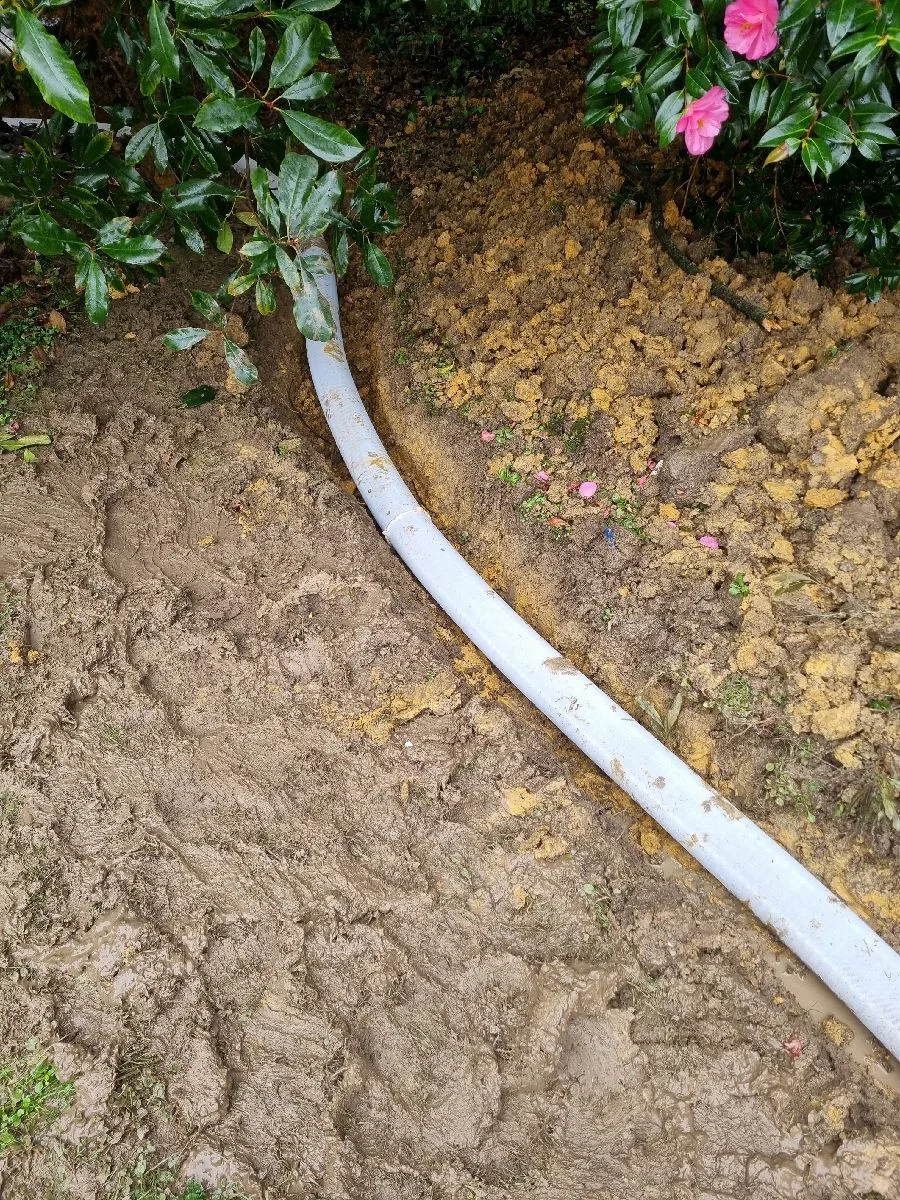 New drainage pipe laid in a trench through a garden bed