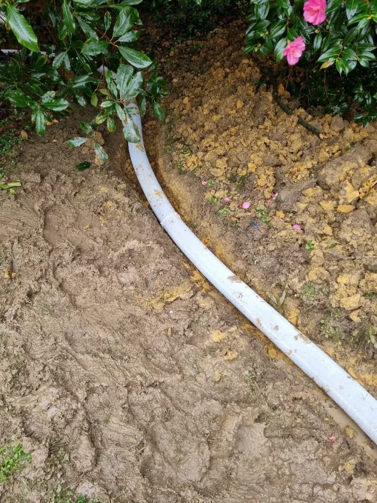 New drainage pipe laid in a trench through a garden bed