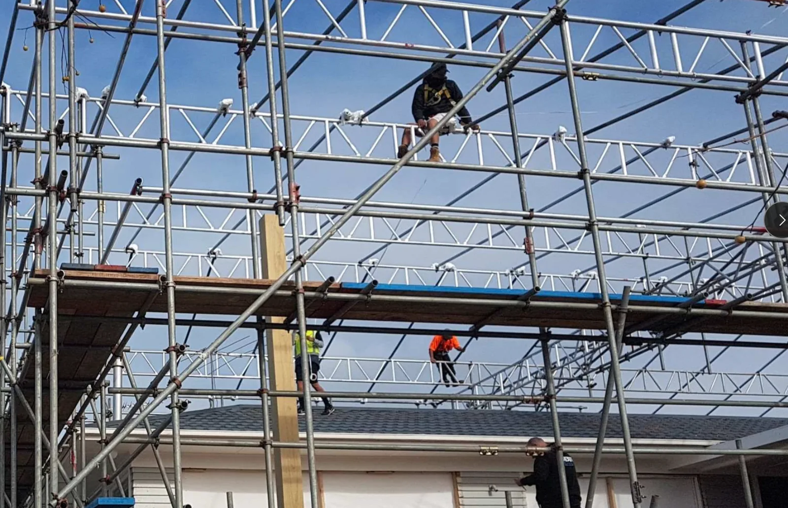 Workers erecting scaffolding over a commercial roof structure